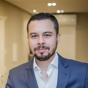 Retrato do Dr. Lucas Tadeu Moura de jaleco branco e gravata, com os braços cruzados